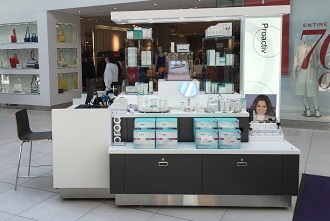 Chariot blanc de soins de la peau Proactiv présentant des produits en boîte, avec un tabouret à côté.