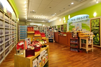 Intérieur de la boutique Tea Desire avec des planchers de bois, des murs verts et des étagères garnies de boîtes de thé et de coffrets-cadeaux.