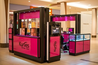 Kiosque rose et noir de Kurves Brow Bar avec des images beauté rétroéclairées et des vitrines en verre.